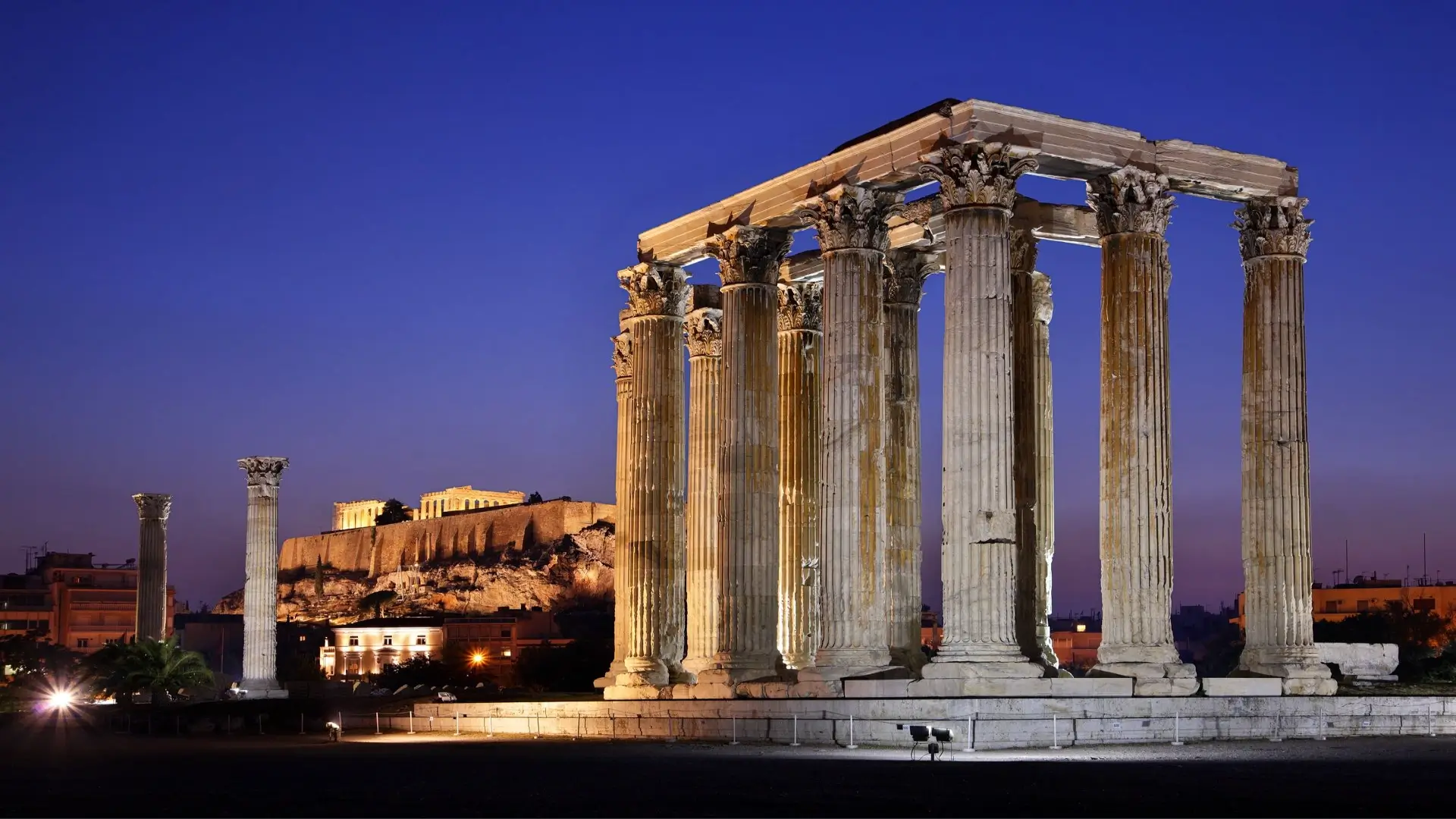 Image of the Temple of Olympian Zeus at night. The Acropolis Hill can be seen in the background.